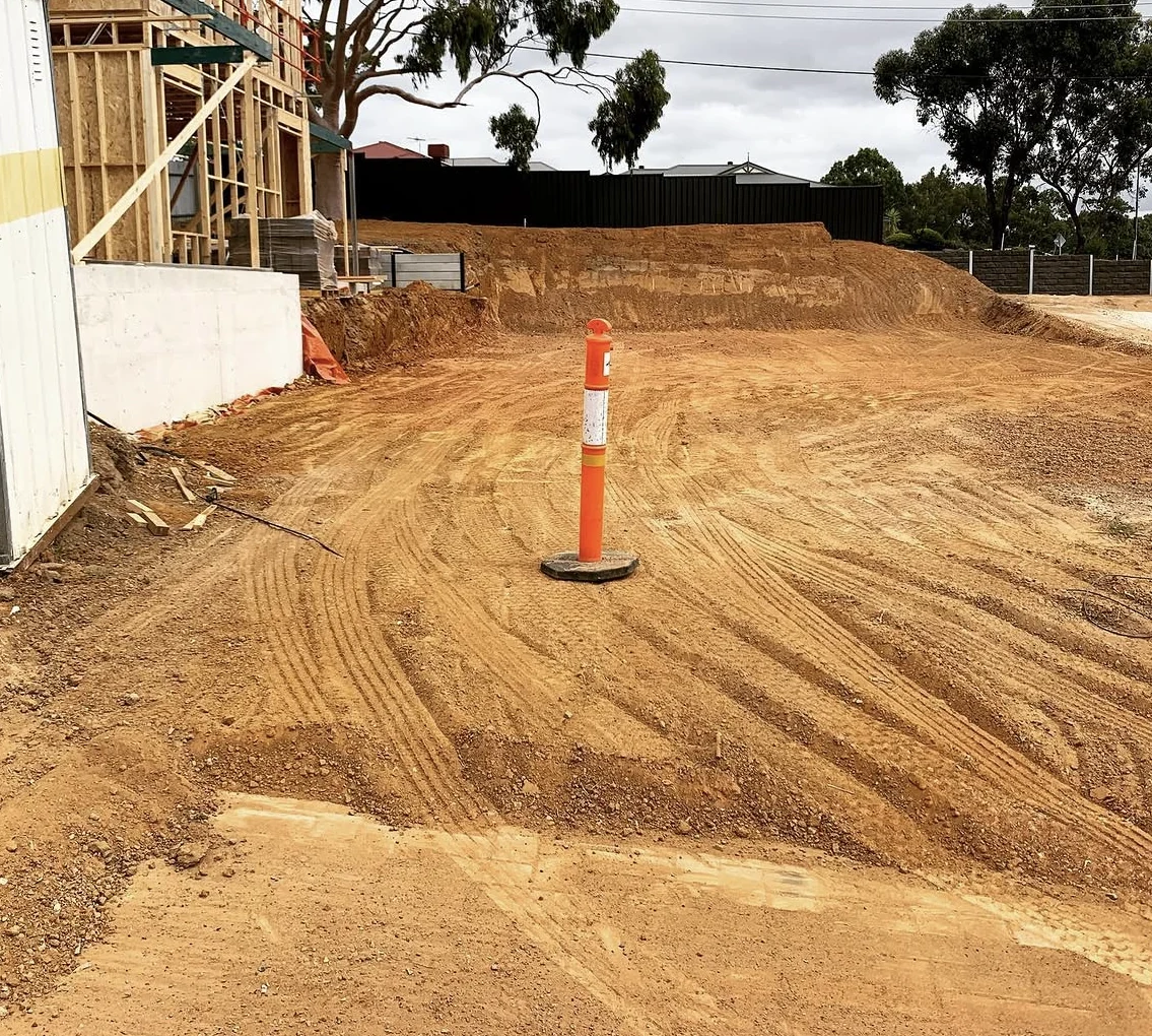 Deep residential site cut beside a house under construction, with exposed earth levels