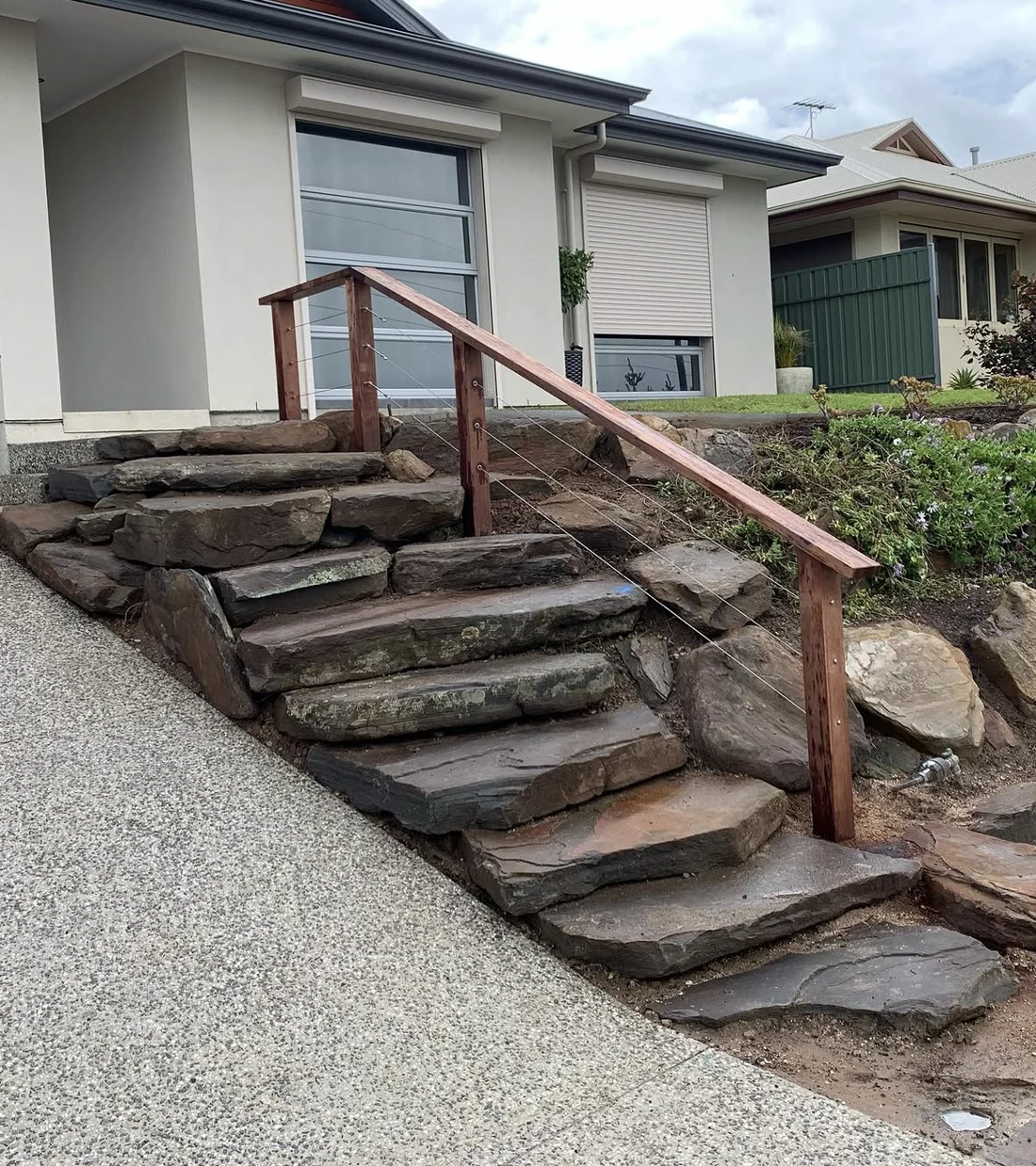 Natural stone staircase, timber rail and planting connecting a sloping front garden
